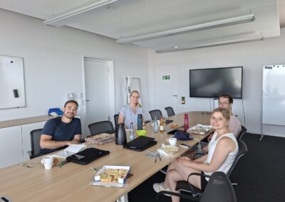Personen sitzen an großen Besprechungstisch aus Holz, weiße Wände, es wurde Essen bestellt