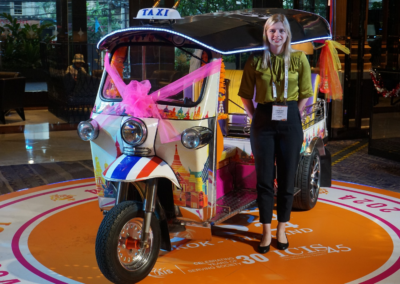 Fabienne Schnieders, Frau mit blonden Haaren, steht neben einem Tuk Tuk auf einer Konferenz in Thailand