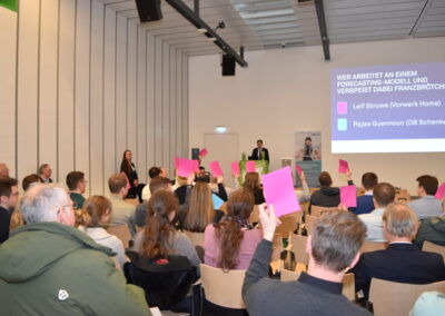 Planum beim Neujahrsempfang, Menschen sitzen auf Holzstühlen und halten pinke Karten hoch