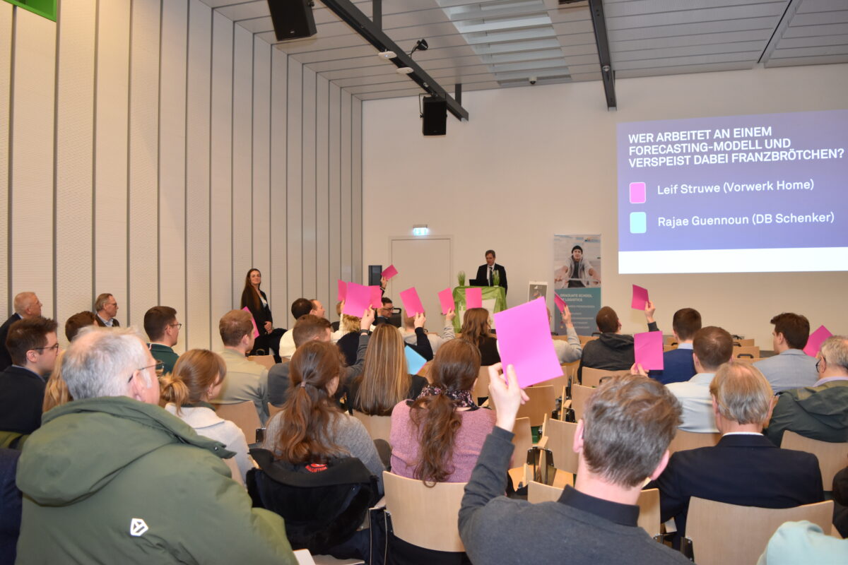 Planum beim Neujahrsempfang, Menschen sitzen auf Holzstühlen und halten pinke Karten hoch