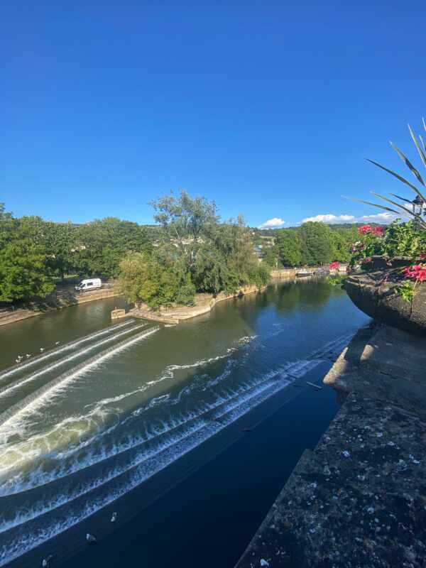 Fluss durch Bath, England, Stufen bilden kleine Wasserfälle, Bäume, blauer Himmel