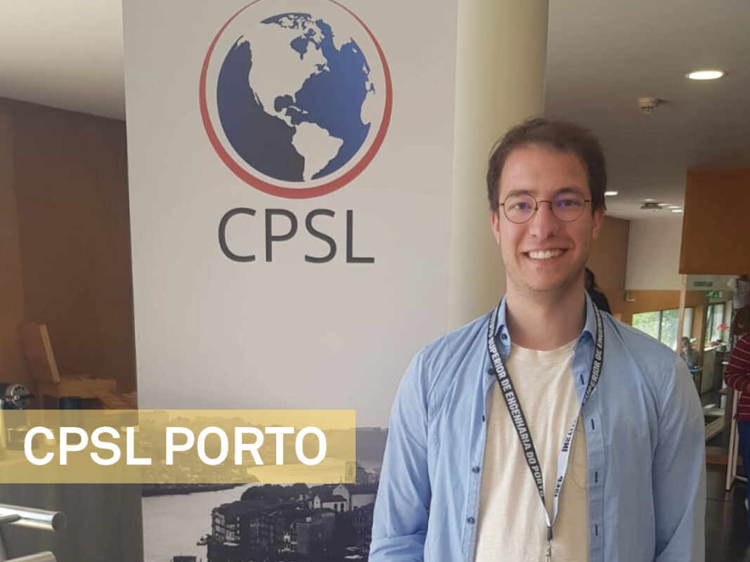 Foto von Jakob Becker, Mann bin dunkelblonden Haaren, blauem Hemd und weißem T-shirt, trägt Namensschild um den Hals, Roll-up mit CPSL-Logo