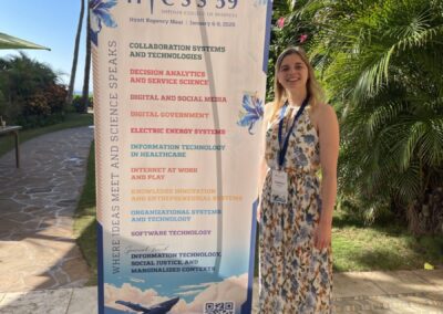 Fabienne Schnieders steht im langen Kleid vor einem Banner der HICSS Konferenz auf Hawaii