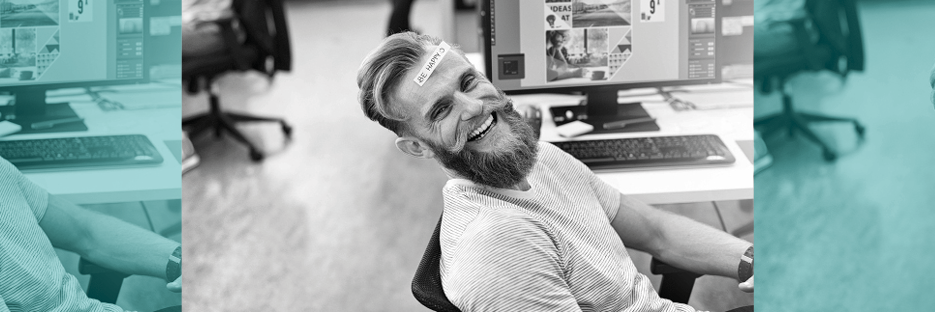 Junger Mann im Büro lacht mit Post-it an der Stirn "Be happy"