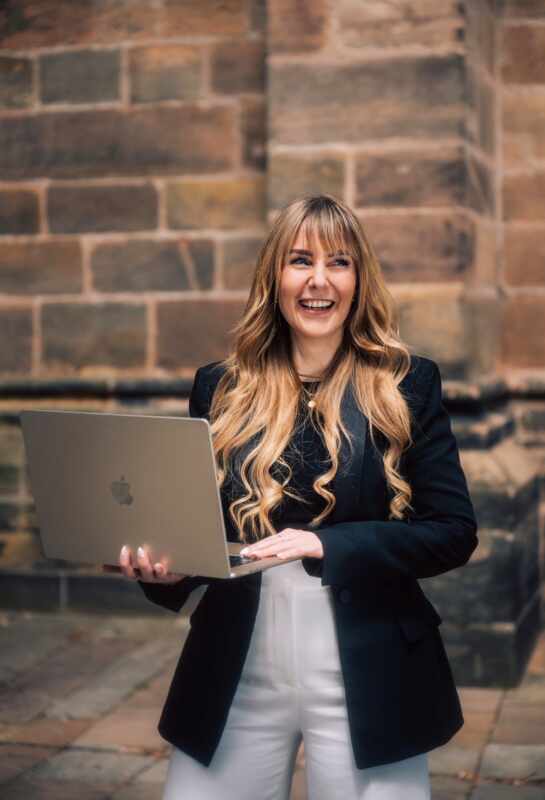 Foto von Isabel Bücker, Frau mit blonden, langen Haaren, Pony, schwarzer Blazer, hält Laptop in der Hand