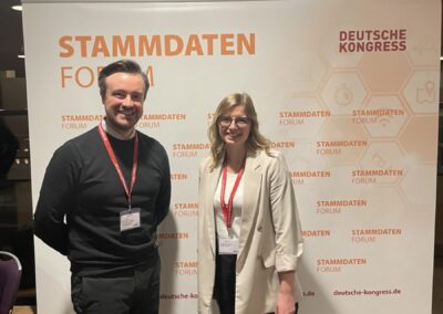 Fabienne Schnieders steht vor einem Werbebanner des Stammdatenforums, weiß mit orangener Schrift