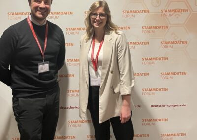 Fabienne Schnieders steht vor einem Werbebanner des Stammdatenforums, weiß mit orangener Schrift